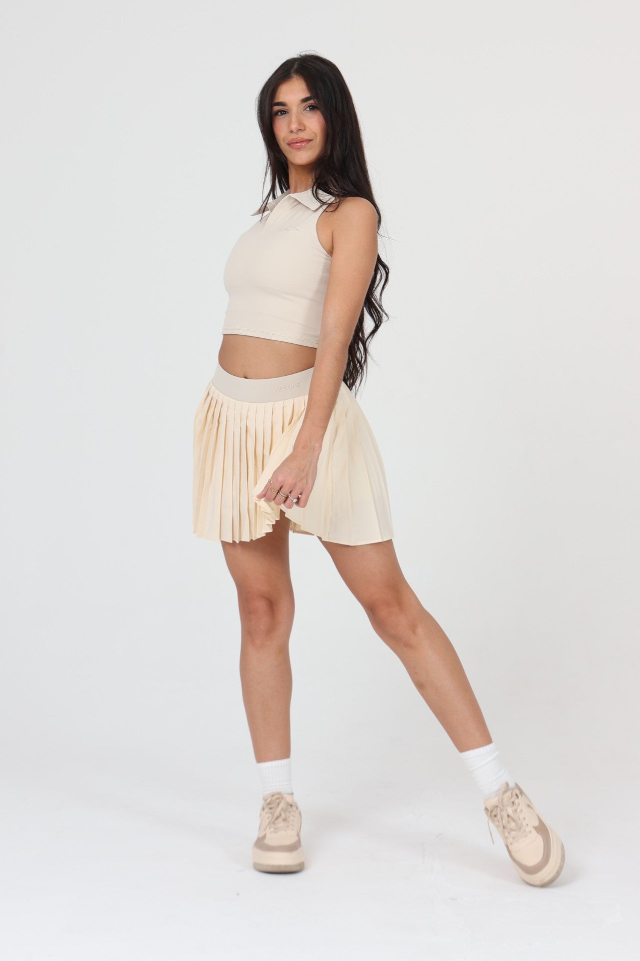 Woman reaching for a lob in ACE ONE beige pleated padel skirt