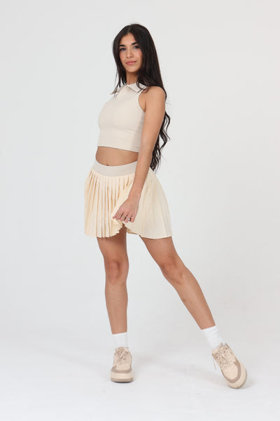 Woman reaching for a lob in ACE ONE beige pleated padel skirt